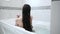 Young woman brunette with long hair takes bath and washes her hair sitting in bathtub