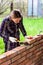 Young woman builds a wall of bricks, lays a brick on a cement-sand mortar, tapping a brick with a hammer.