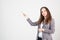 young woman in business formal clothes poses against a white wall and points at something