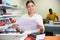 Young woman calculates the cost of printed notepads and sheet in the typography