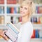 Young Woman Carrying Stacked Books In Library