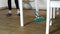 Young woman in casual outfit doing chores at home using modern broomstick to sweep the floor in kitchen. Legs of a young