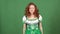 Young woman celebrating saint patrick`s day on green wall wearing traditional dress changing hair volume