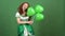 Young woman celebrating saint patrick`s day on green wall wearing traditional dress holding balloons