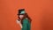 Young woman celebrating saint patrick`s day on orange wall in hat greedy leprechaun