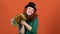 Young woman celebrating saint patrick`s day on orange wall in hat shaking pom poms