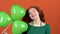 Young woman celebrating saint patrick`s day on orange wall holding clover-shaped balloons