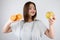 Young woman with centimeter round her neck looking at apple in her hand wih two half of oranges in another isolated white