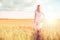 Young woman with cereal spikelets walking on field