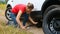 Young woman changing flat tire on car broken at field