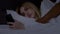 Young woman chatting on smartphone in family bed, pretending sleeping when her black husband waking up in night