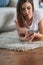 Young woman checking her smart phone lying on carpet