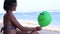 Young woman cheerfully sitting on the beach with green balloon. Bali, Indonesia. Full HD, 50fps. Near the ocean