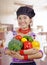 Young woman chef wearing traditional andean blouse, black cooking hat, holding broccoli, capsicum, tomato and lemon