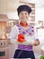 Young woman chef wearing traditional andean blouse, black cooking hat, holding up red capsicum for camera smiling