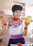 Young woman chef wearing traditional andean blouse, black cooking hat, holding up yellow capsicum for camera smiling