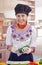 Young woman chef wearing traditional andean blouse, black cooking hat, vegetables on desk, shredding cucumber into deep