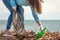 A young woman on a clean-up of the coastal area, collecting garbage. Sea and sky in the background. Earth day and ecology