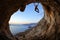 Young woman climbing on ceiling in cave at sunset