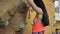 Young woman climbs on climbing wall, grabbing on stones indoor.