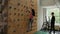 Young woman climbs on climbing wall under supervision of instructor indoors.