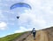 A young woman climbs up a mountain to meet a paraglider hovering in the air