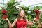 Young woman with closed eyes in a red dress in a greenhouse among lush tropical plants holds a poinsettia flowers in both hands