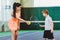 Young woman or coach teaching child how to play tennis on a court indoor