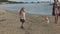 Young woman in a coat with a girl with curly hair, mom and daughter, run, play with a brown dog on the beach, brood her