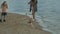 Young woman in a coat with a girl with curly hair, mom and daughter, run, play with a brown dog on the beach, brood her