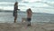 Young woman in a coat with a girl with curly hair, mom and daughter, run, play with a brown dog on the beach, brood her