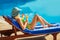 Young woman with cocktail glass near swimming pool on a deck chair