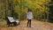 Young woman collects her bunch of yellow leaves and takes a seat on a bench