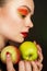 Young woman with colored make-up holds apples.