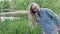 Young woman combs a long fair hair on the bank of the lake in sunny day