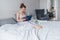 Young woman in comfortable lilac pajamas works the computer while lying on bed in bedroom