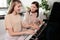Young woman consulting her clever teenage daughter while both sitting by piano