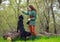 Young woman in country style clothes exercises with black retriever dog in spring forest