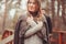 Young woman in cozy warm cardigan walking outdoor in autumn forest, with boyfriend on background