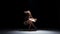 Young woman dancer dancing contemporary dance moves, jumps and makes a split, on black, shadow