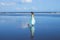 Young woman dancing barefoot on empty sandy beach. Full body portrait. Slim Caucasian woman wearing long dress. Water reflection.