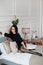 Young woman with dark hair in black dress and round stylish glasses posing on the bed in a luxury minimalist interior