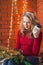 A young woman decorates a house for Christmas and New Year. Drinks cofee. Against the background of a brick wall