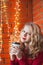 A young woman decorates a house for Christmas and New Year. Drinks cofee. Against the background of a brick wall