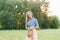 Young woman in a denim shirt and pink skirt holds a hat in her hands, she smiles and walks in nature in the summer