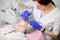 Young woman dermatologist cosmetologist in sterile gloves, applying cream mask on face of her female client for