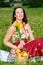 Young woman in dirndl sitting in meadow and holding sunflower