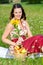 Young woman in dirndl sitting in meadow and holding sunflower