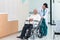 Young woman doctor with senior man sitting on wheelchair in hospital. female doctor assist take care of smiling old man. elderly