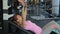 Young woman doing barbell bench press under trainer supervision in gym. Female lies on bench.